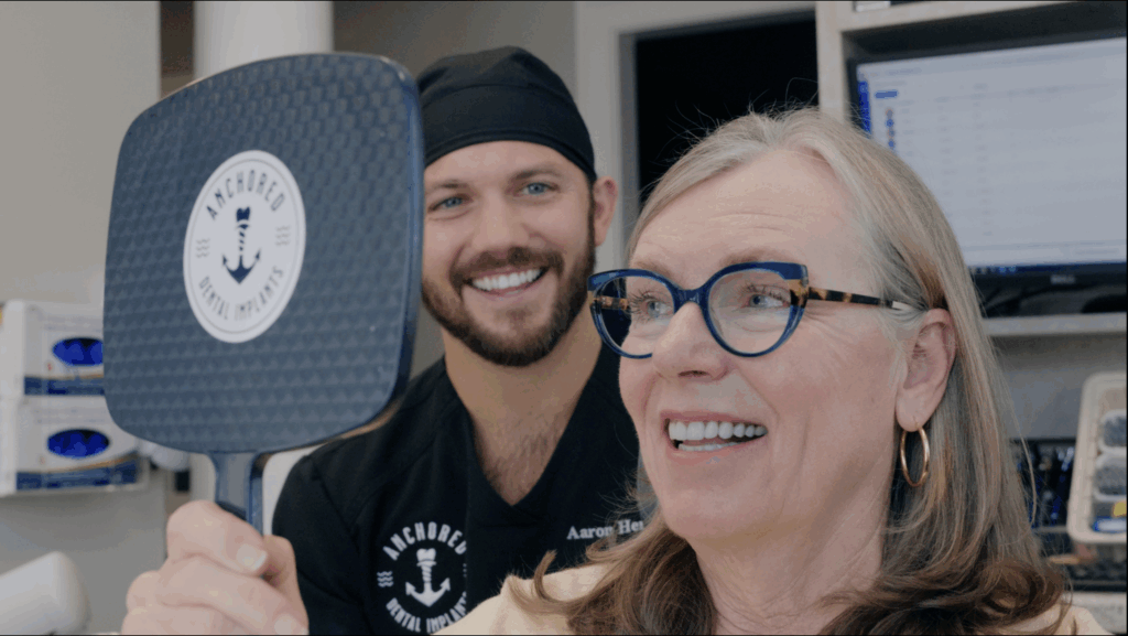 Woman with new full-mouth dental implants looking in mirror with her new smile